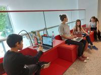 3 Kinder und eine Erwachsene auf roten Sitzen mit Laptops